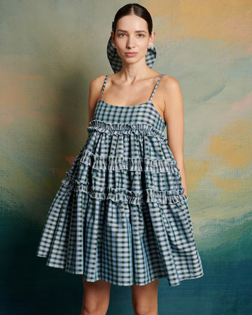 model wearing blue gingham mini dress with adjustable straps and ruffle tier detail