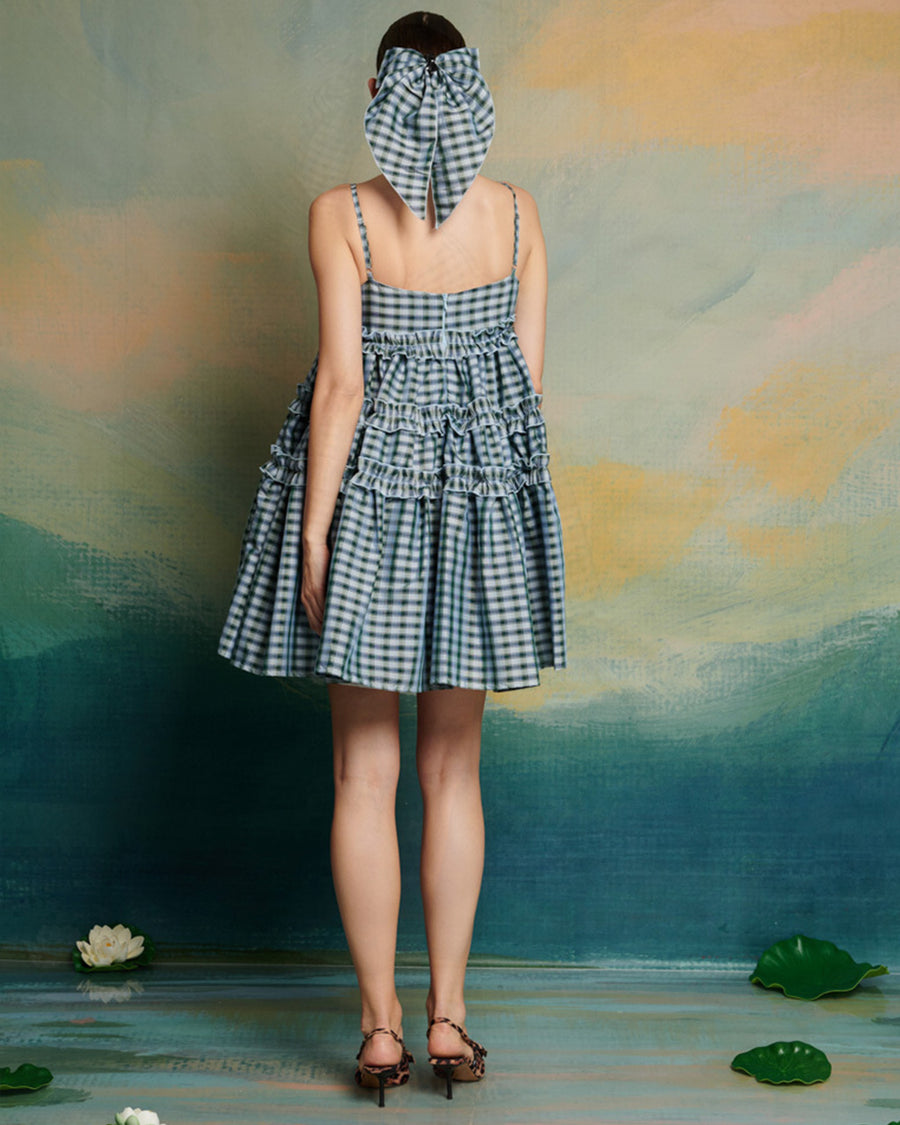 back view of model wearing blue gingham mini dress with adjustable straps and ruffle tier detail