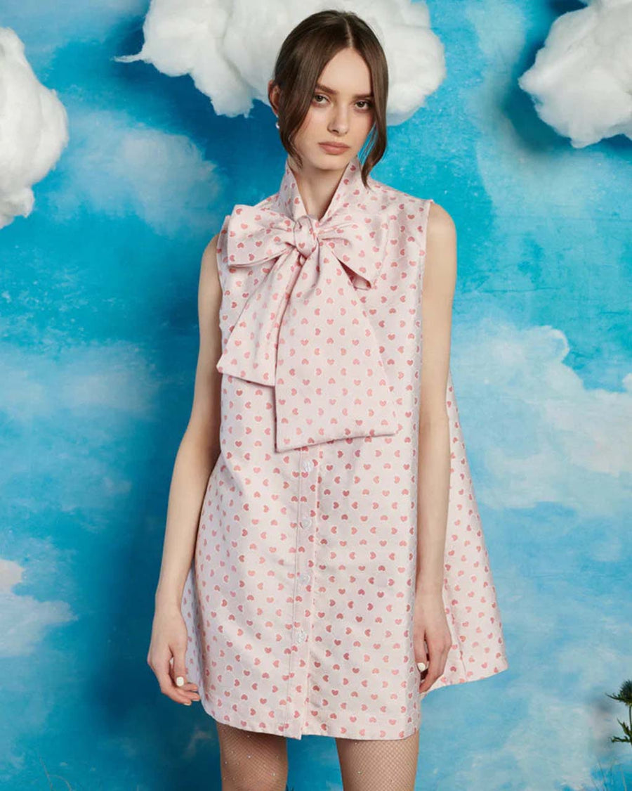 model wearing light pink mini dress with all over pink heart print and oversized bow