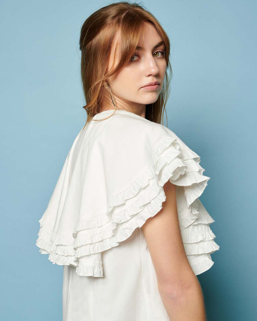 up close of model wearing white mini dress with oversized ruffle cape top