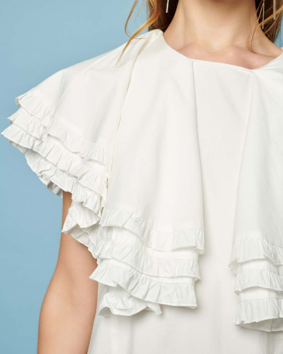 up close of front of model wearing white mini dress with oversized ruffle cape top