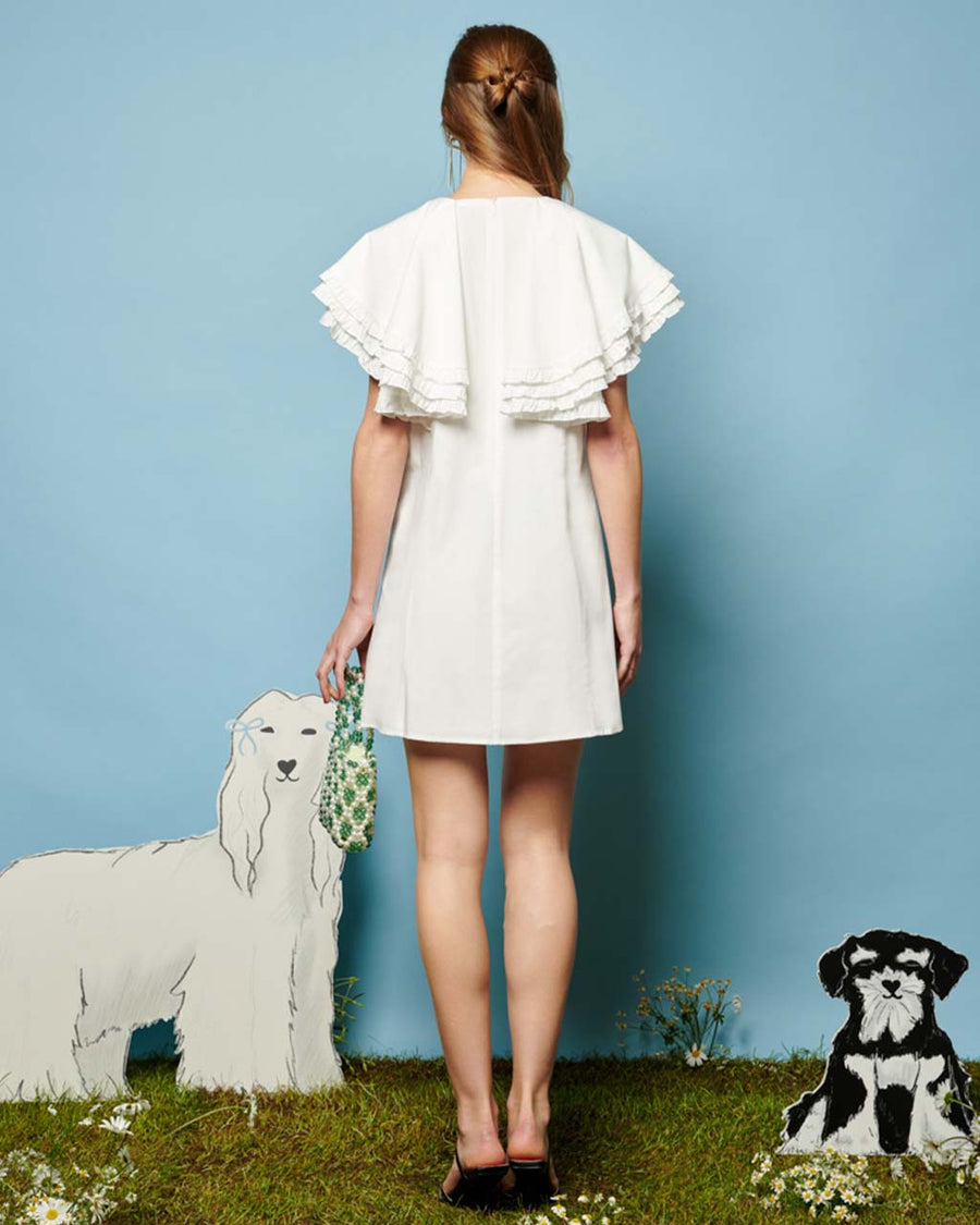 back view of model wearing white mini dress with oversized ruffle cape top