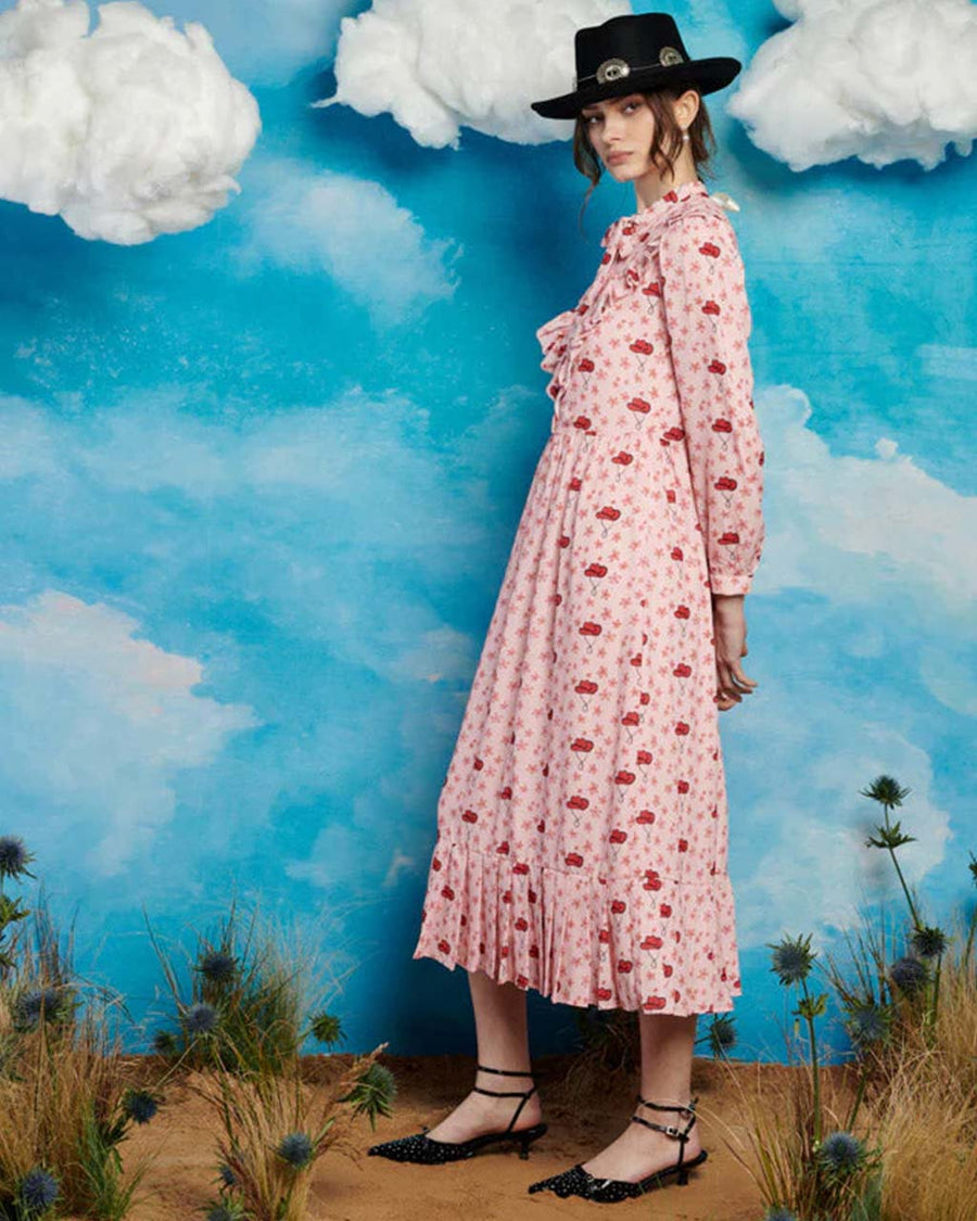 side view of model wearing light pink midi dress with long sleeves, front yoke and tie and pink cowboy hat print