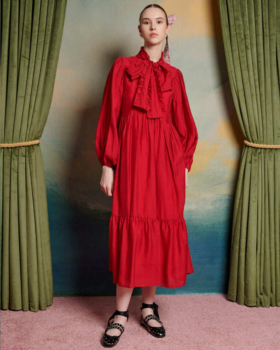 model wearing red midi dress with oversized tie neckline, slight puff long sleeves and tiered skirt