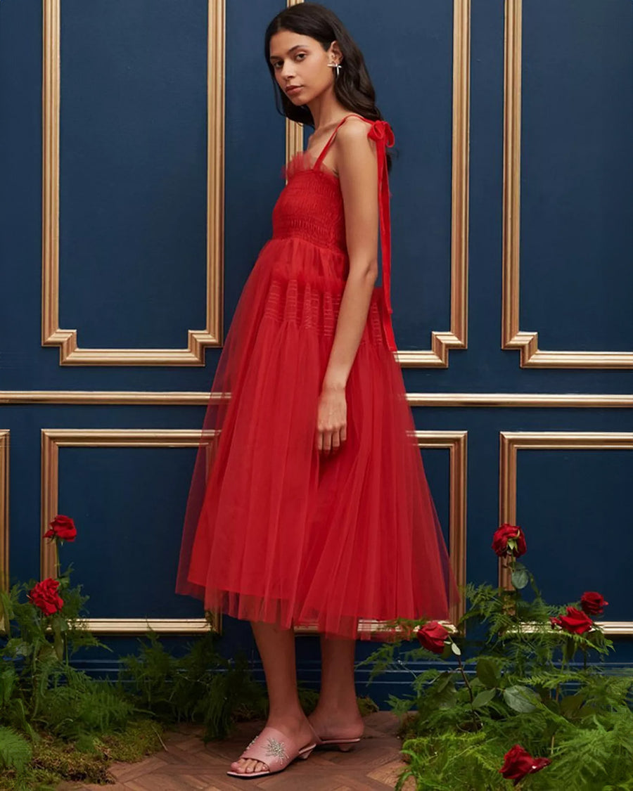 side view of model wearing red tulle midi dress with velvet tie straps and smocked bodice