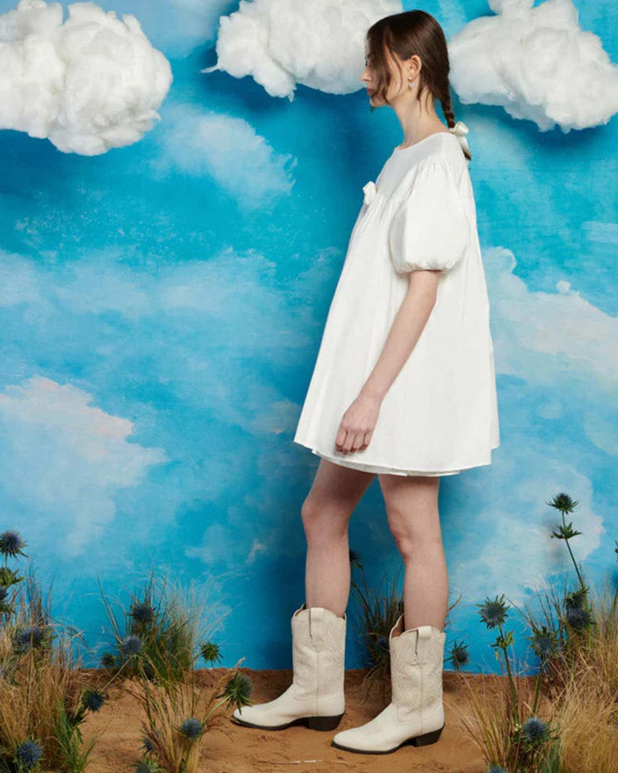 side view of model wearing white mini dress with puff sleeves and removable rose pin in the front