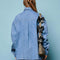 back view of model wearing washed denim long sleeve top with oversized bow on the neckline, front pocket and relaxed fit