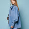 side view of model wearing washed denim long sleeve top with oversized bow on the neckline, front pocket and relaxed fit