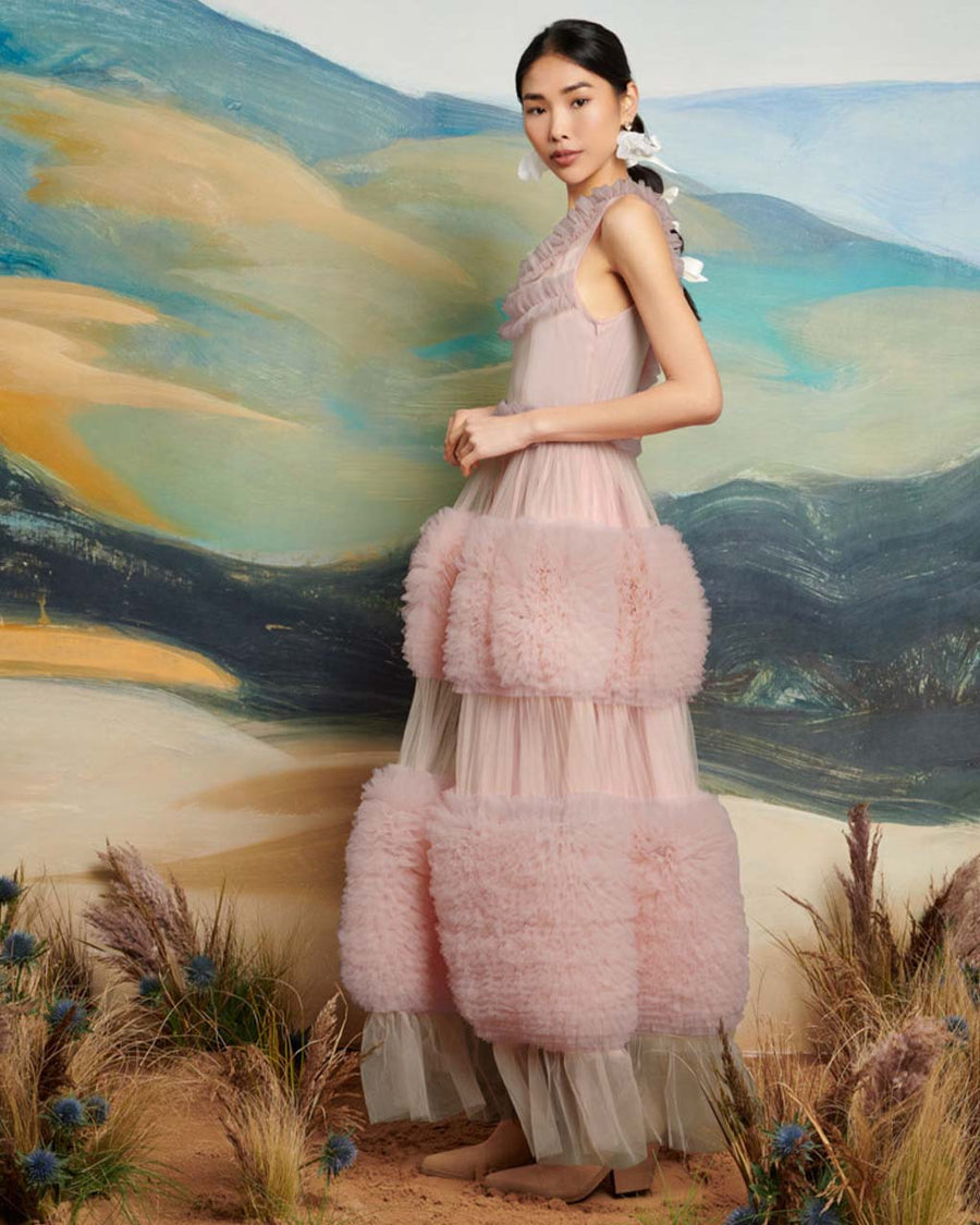 side view of model wearing mauve midi dress with a fitted waist in a soft tulle fabric, fully lined and detailed with a voluminous skirt and layered tulle ruffles with a raw edge.