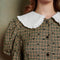 up close of model wearing green check and heart print midi dress with puff sleeves and white oversize collar, and button front