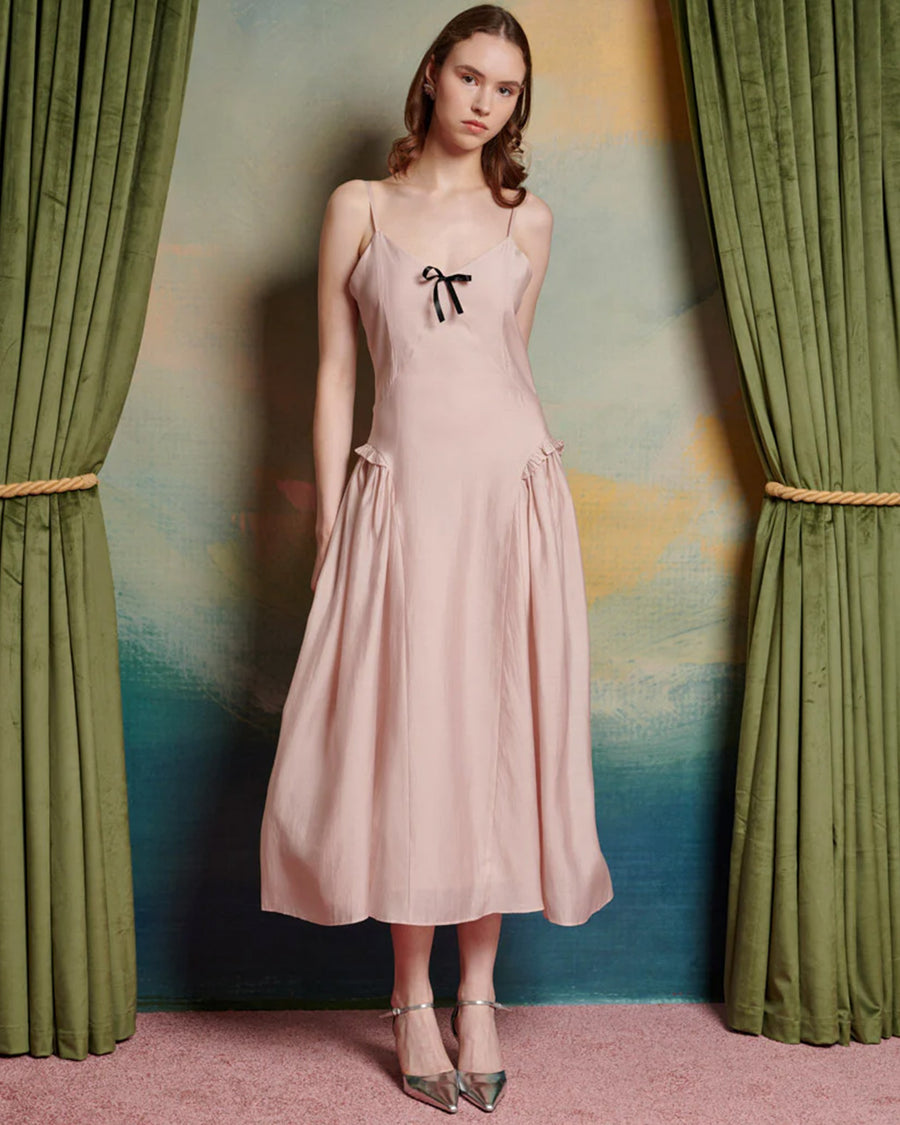 model wearing light pink midi dress with black bow on the bust and ruffle material on the hips