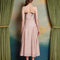 back view of model wearing light pink midi dress with black bow on the bust and ruffle material on the hips