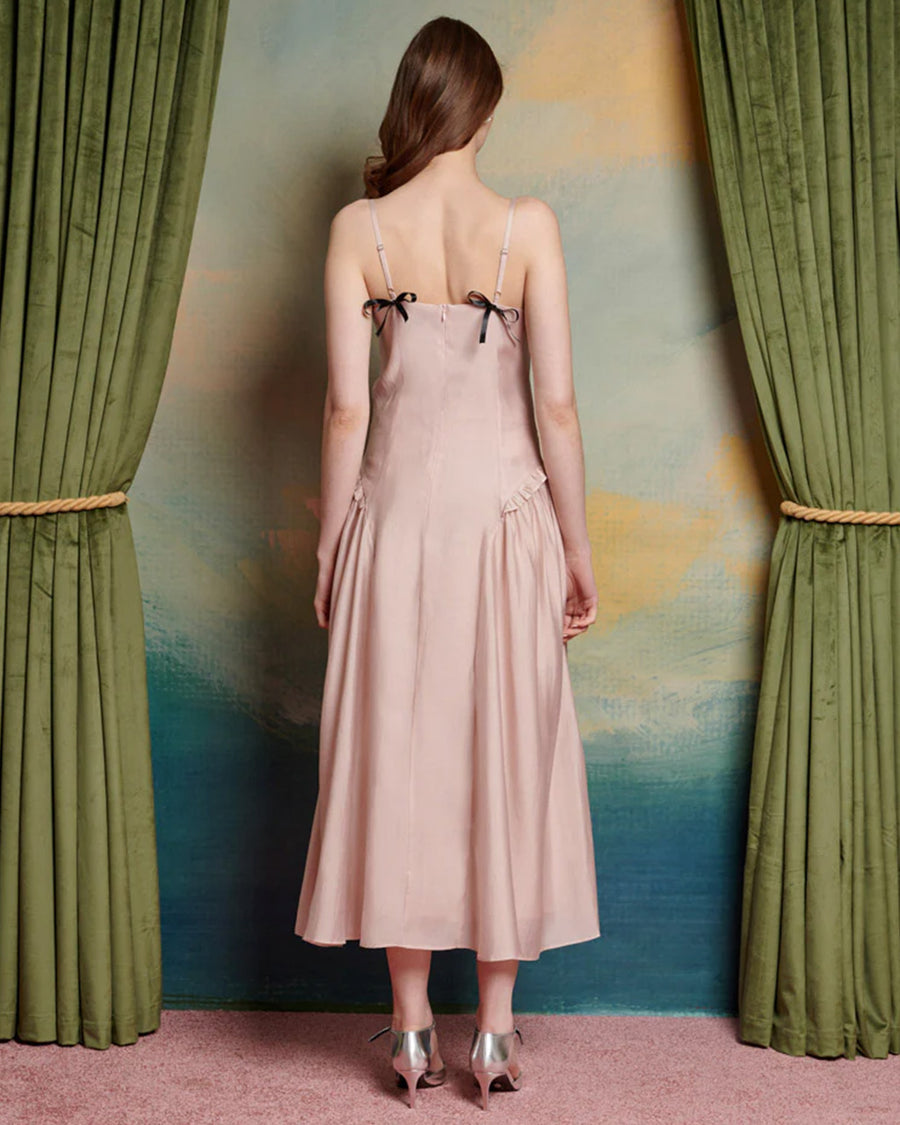 back view of model wearing light pink midi dress with black bow on the bust and ruffle material on the hips