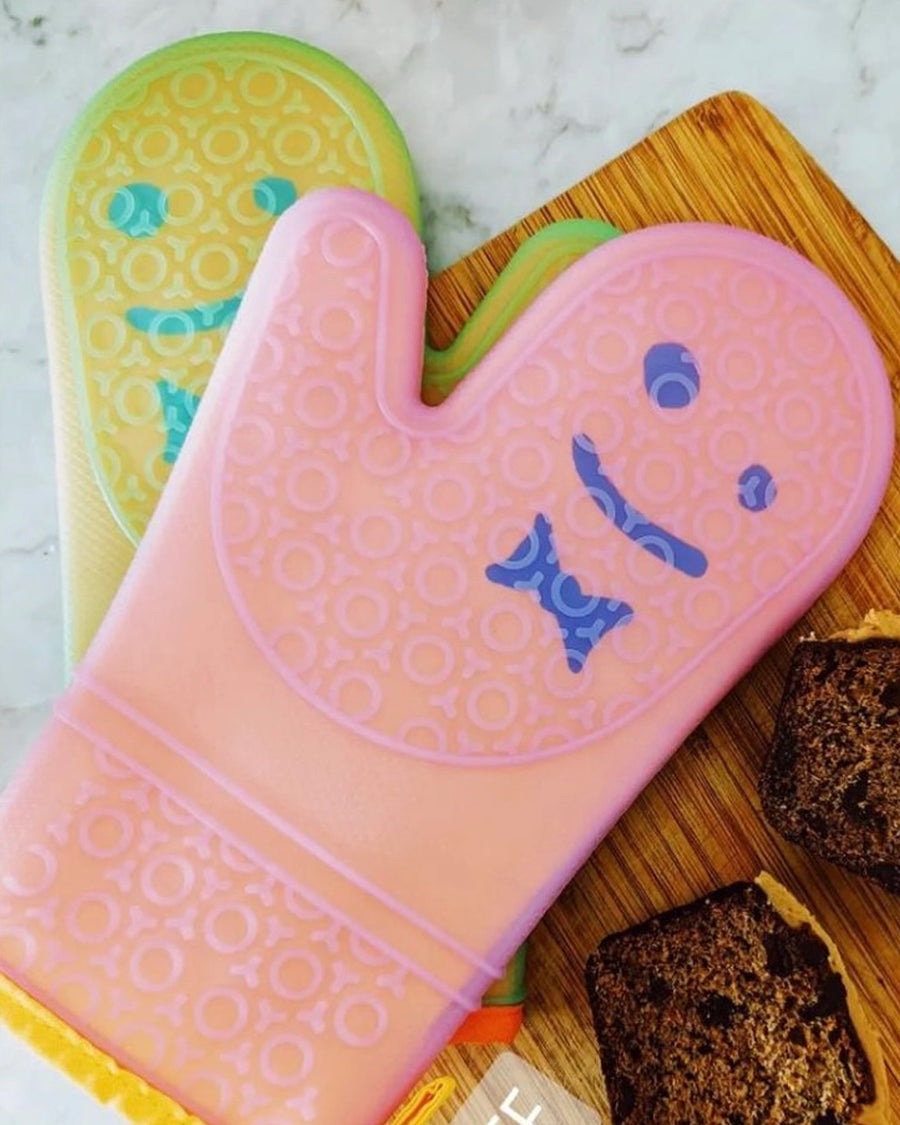 set of 2 orange and pink silicone oven mitts with smiley face detail on a cutting board