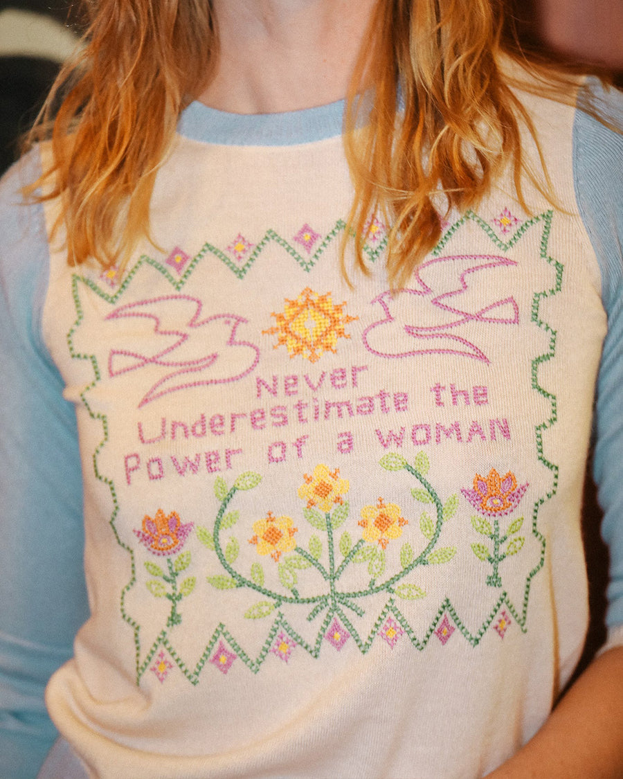 model wearing white sweater with blue sleeves and trim with colorful embroidered 'never underestimate the power of a woman'