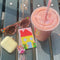 beaded cardholder with yellow house and pink background on a table with a smoothie, sunglasses, and eye buds