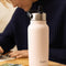 model next to light pink stainless steel water bottle with flip sip lid on a table