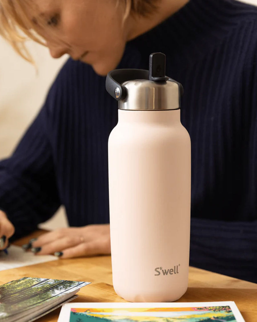 model next to light pink stainless steel water bottle with flip sip lid on a table