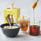 glass honey dipper with birchwood lid, bowl of oatmeal and tea on a table