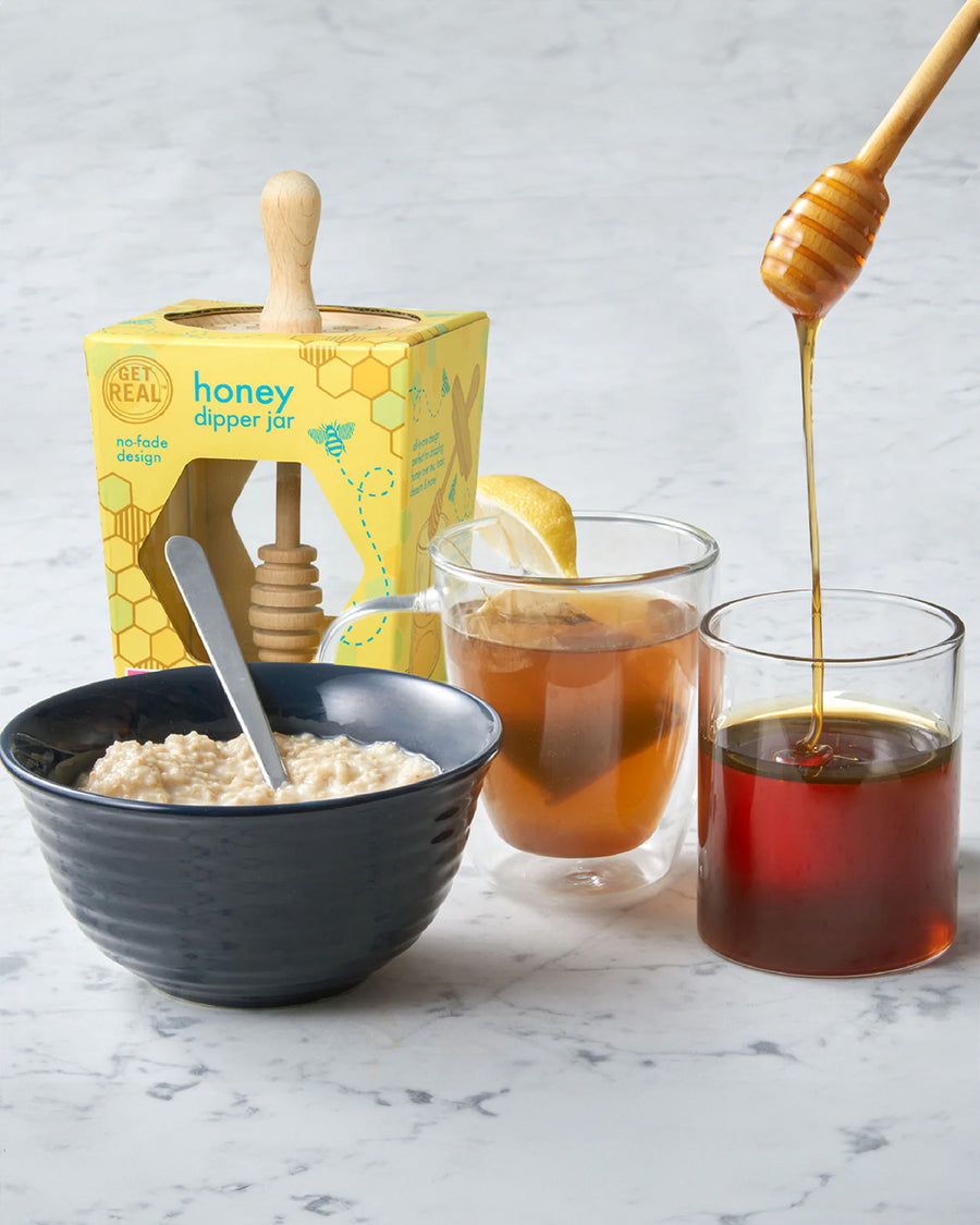 glass honey dipper with birchwood lid, bowl of oatmeal and tea on a table