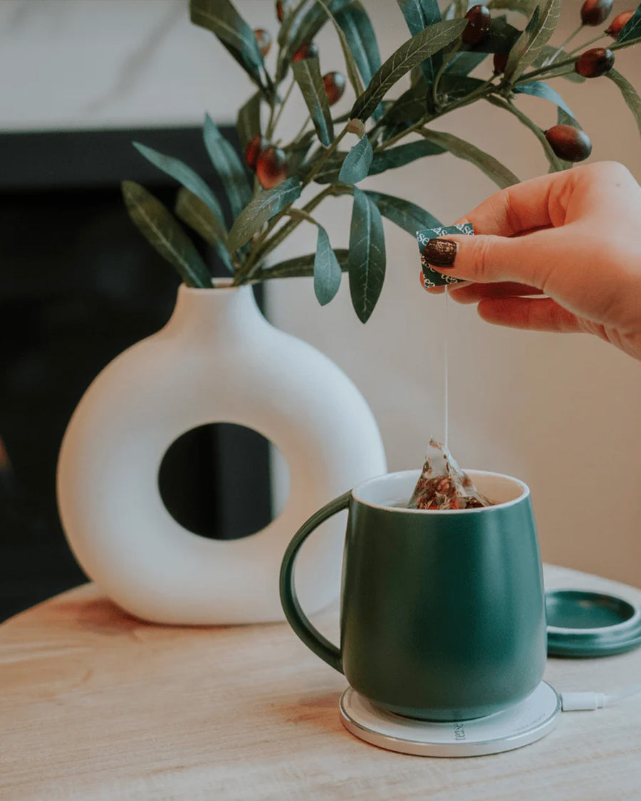 model putting tea bag in dark green smart heated mug set with heat plate