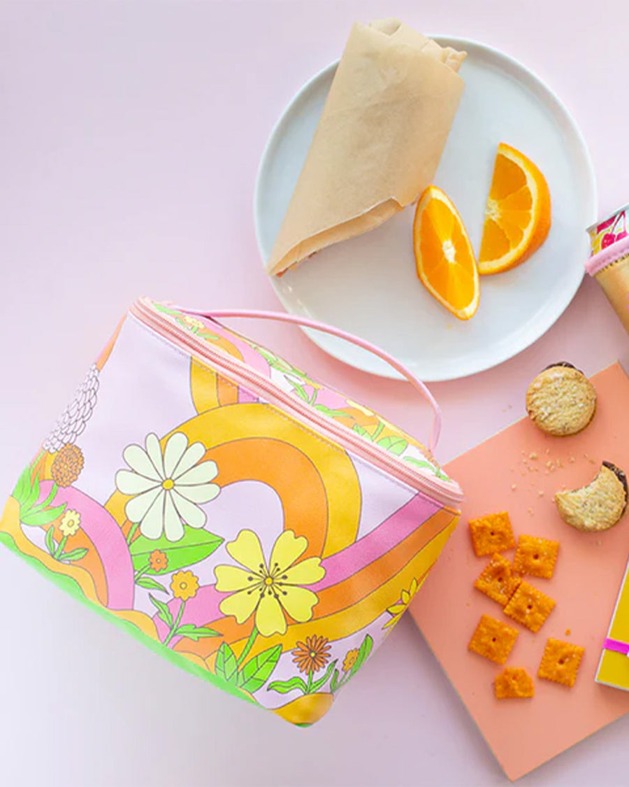 pink pouch with handle and double zippers with colorful 70's type floral print surrounded by snacks and food