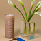 model holding vacation sunscreen lobby candle on a table with a vase of white flowers