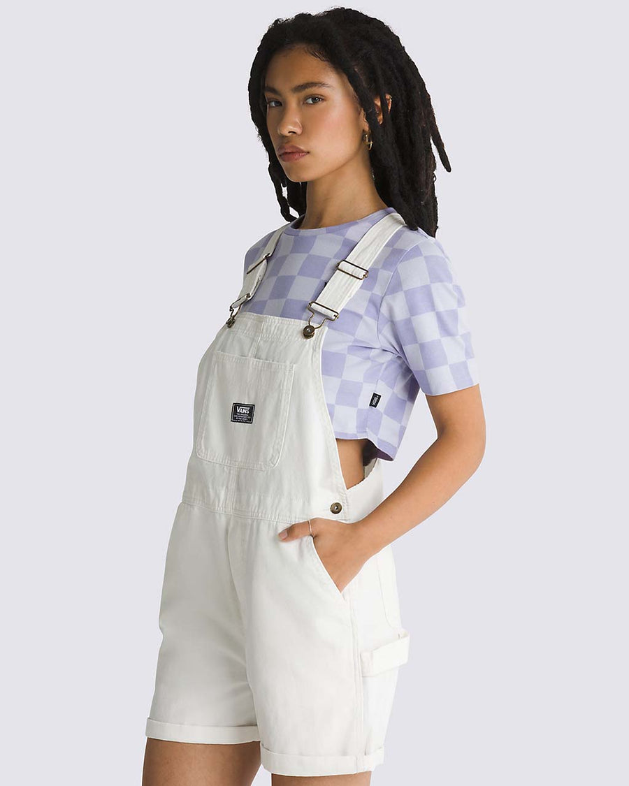 side view of model wearing white cotton short overalls with patch front pocket, adjustable straps, side pockets and vans logo patch