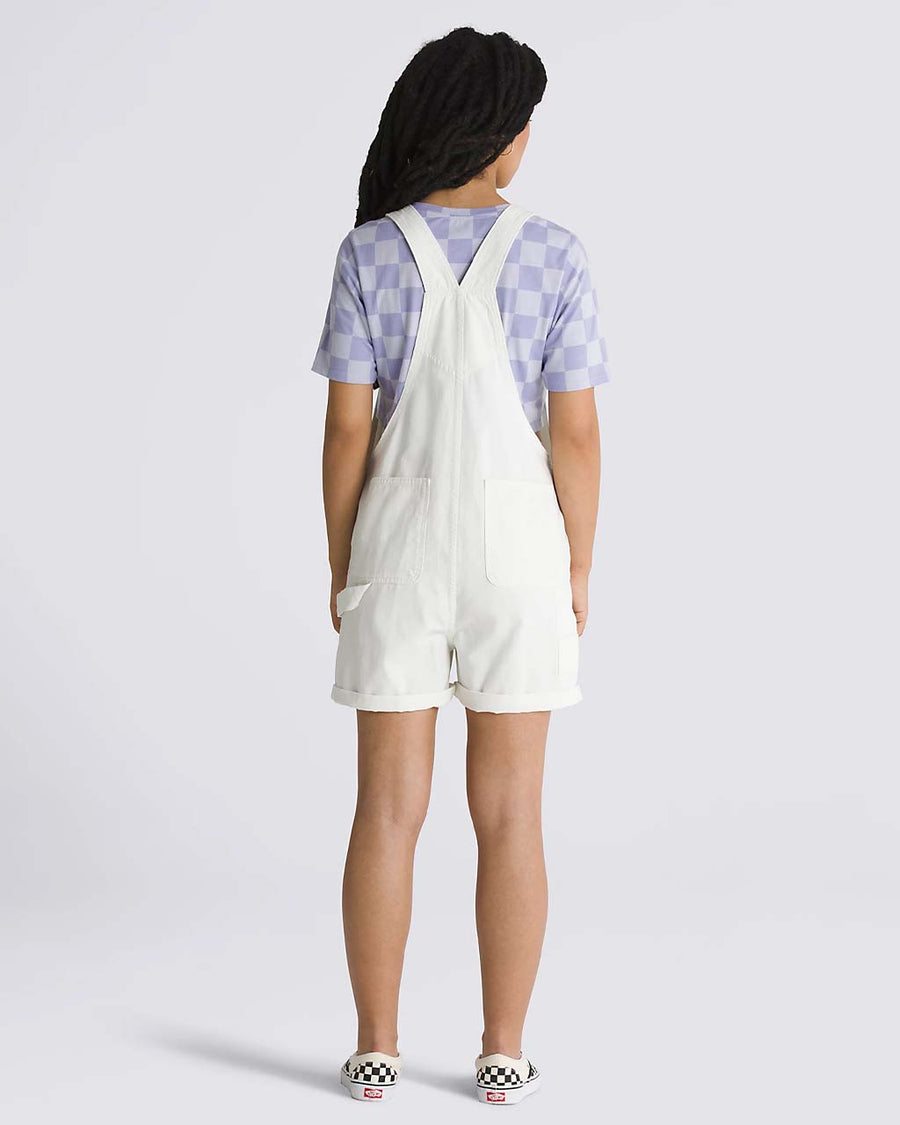 back view of model wearing white cotton short overalls with patch front pocket, adjustable straps, side pockets and vans logo patch