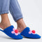 model wearing blue slip on slippers with pink flower and pom detail and fuzzy interior