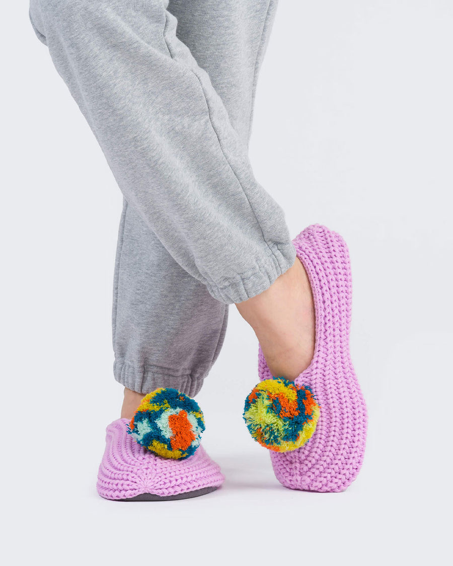 model wearing lilac knitted slip on slipper socks with rainbow pom with their legs crossed