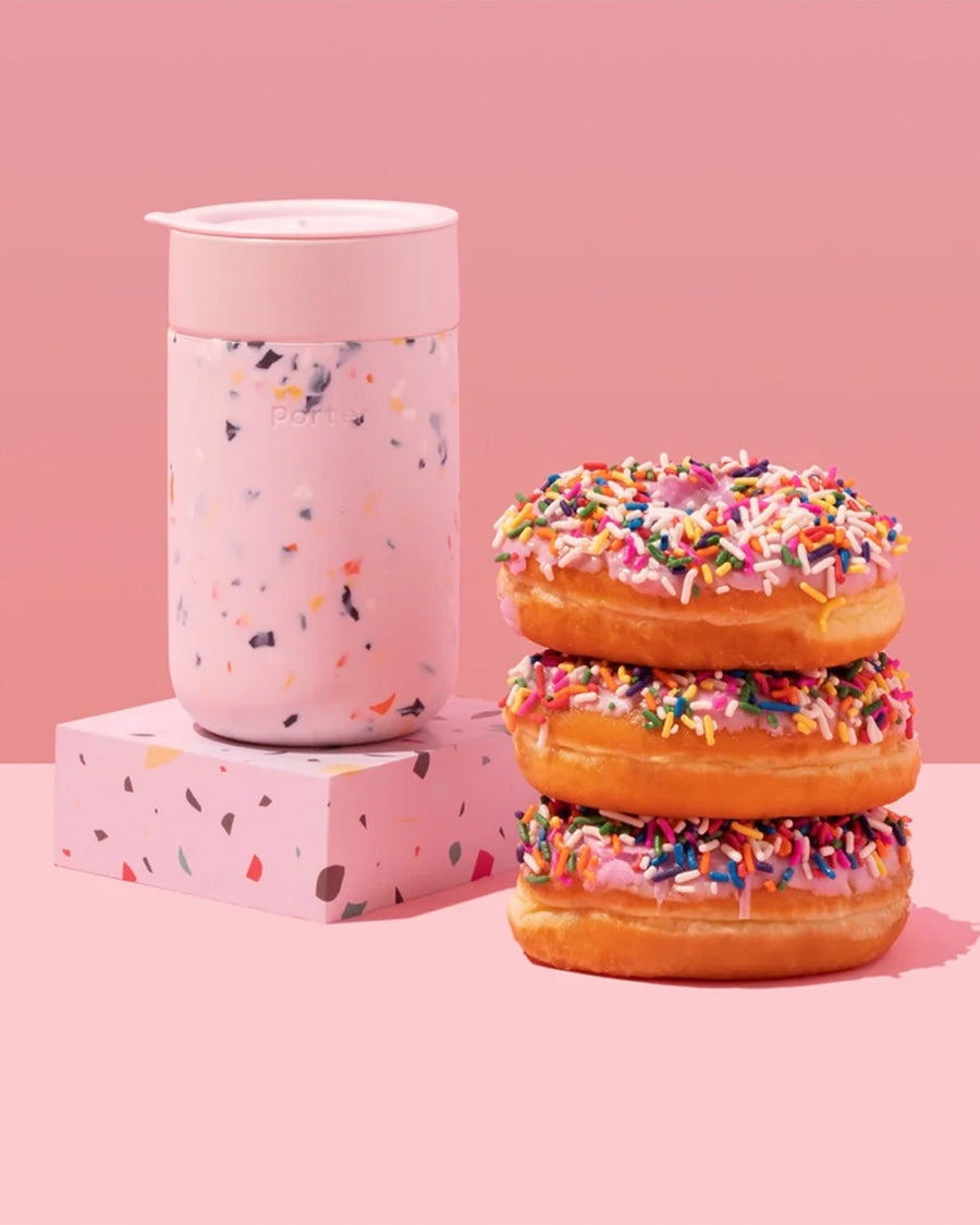 pink terrazzo 16 oz. reusable coffee mug with lid next to a stack of donuts