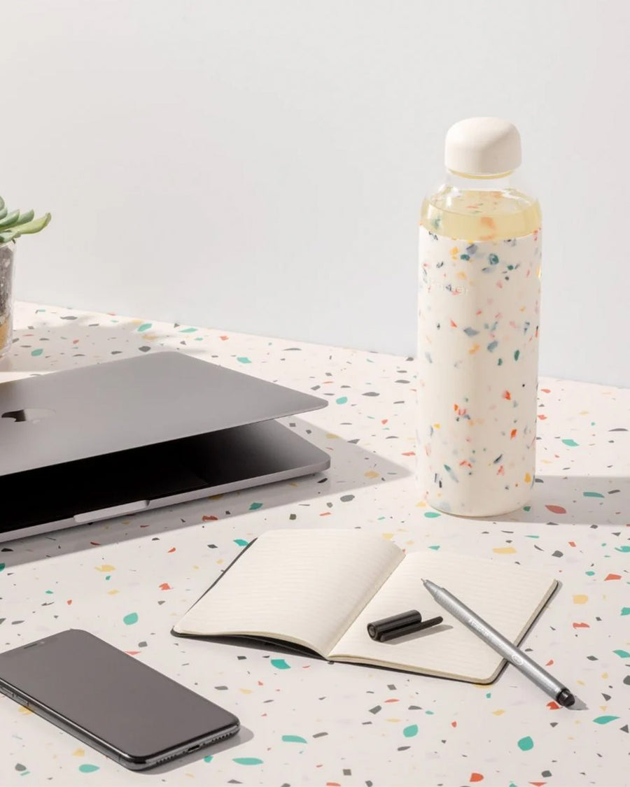 20 oz. glass water bottle with white terrazzo silicone cover on a desk