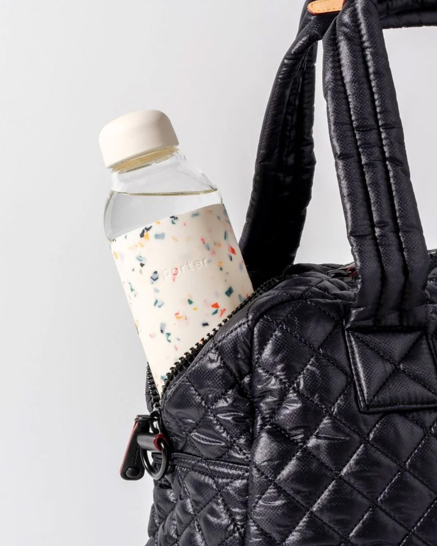 20 oz. glass water bottle with white terrazzo silicone cover sticking out of a bag