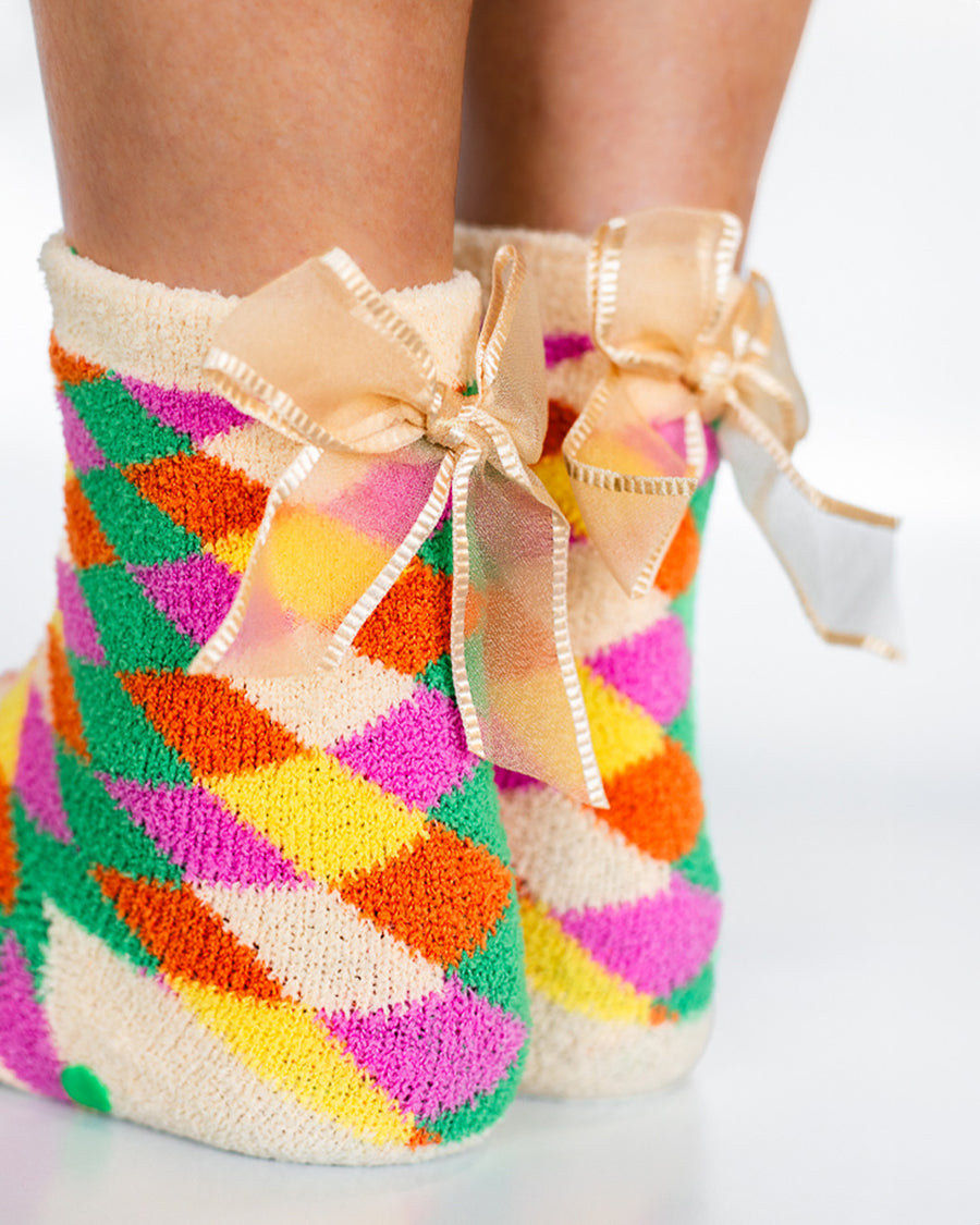 model wearing colorful checkerboard chenille grip socks with removable bow detail