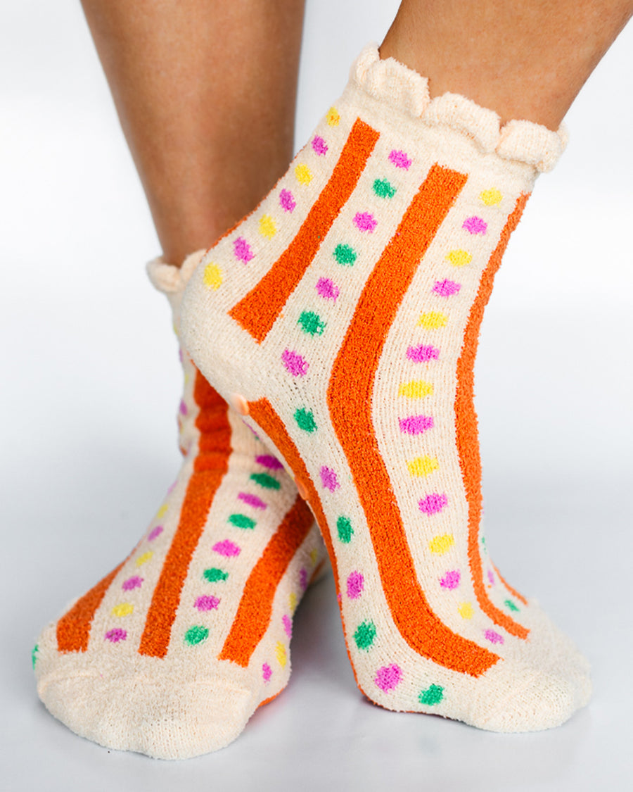 model wearing cream chenille socks with ruffle top with orange stripes and multicolor dots