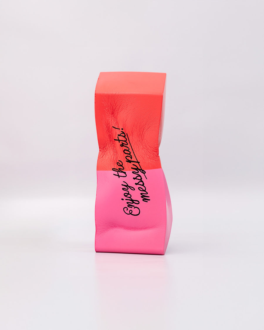 smooshed pink and red eraser shaped de-stress ball with black 'enjoy the messy parts' across the front