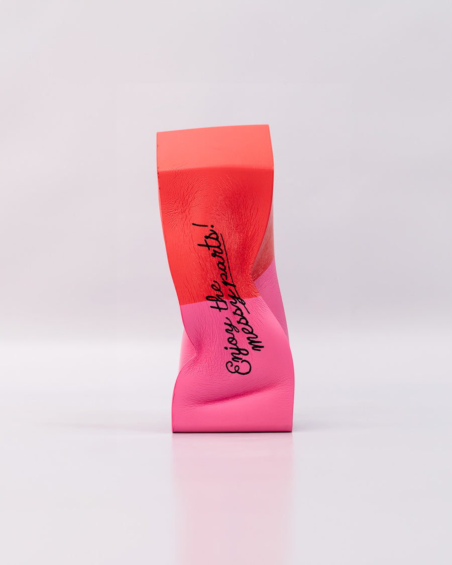 smooshed pink and red eraser shaped de-stress ball with black 'enjoy the messy parts' across the front