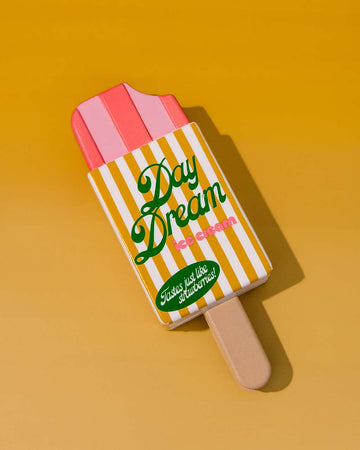 popsicle shaped de-stress ball with yellow and white stripe label that says 'day dream ice cream: tastes like strawberries!' on orange background