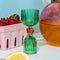 green double shot glass with yellow heart detail near a bowl of strawberries and cherry carafe