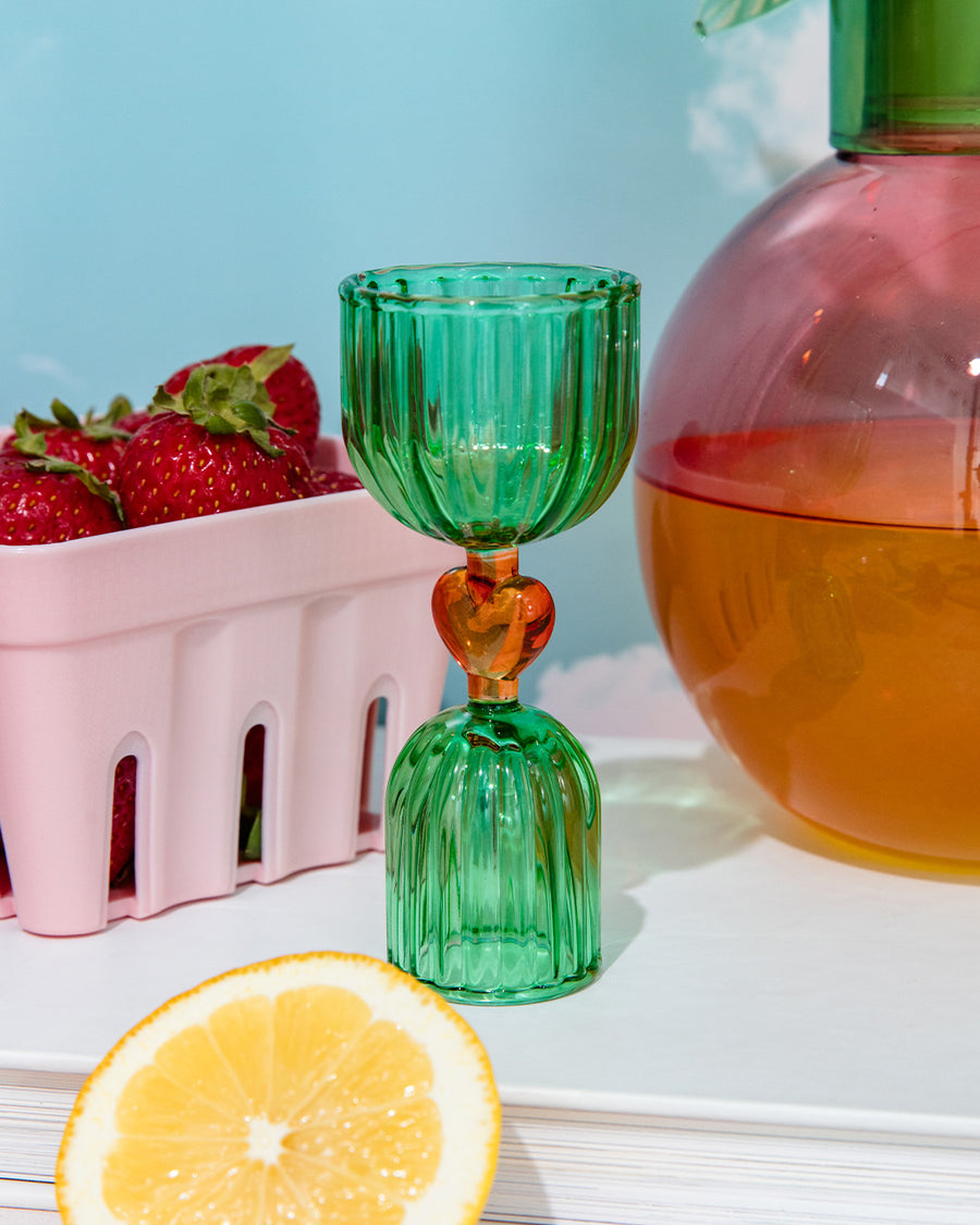 green double shot glass with yellow heart detail near a bowl of strawberries and cherry carafe