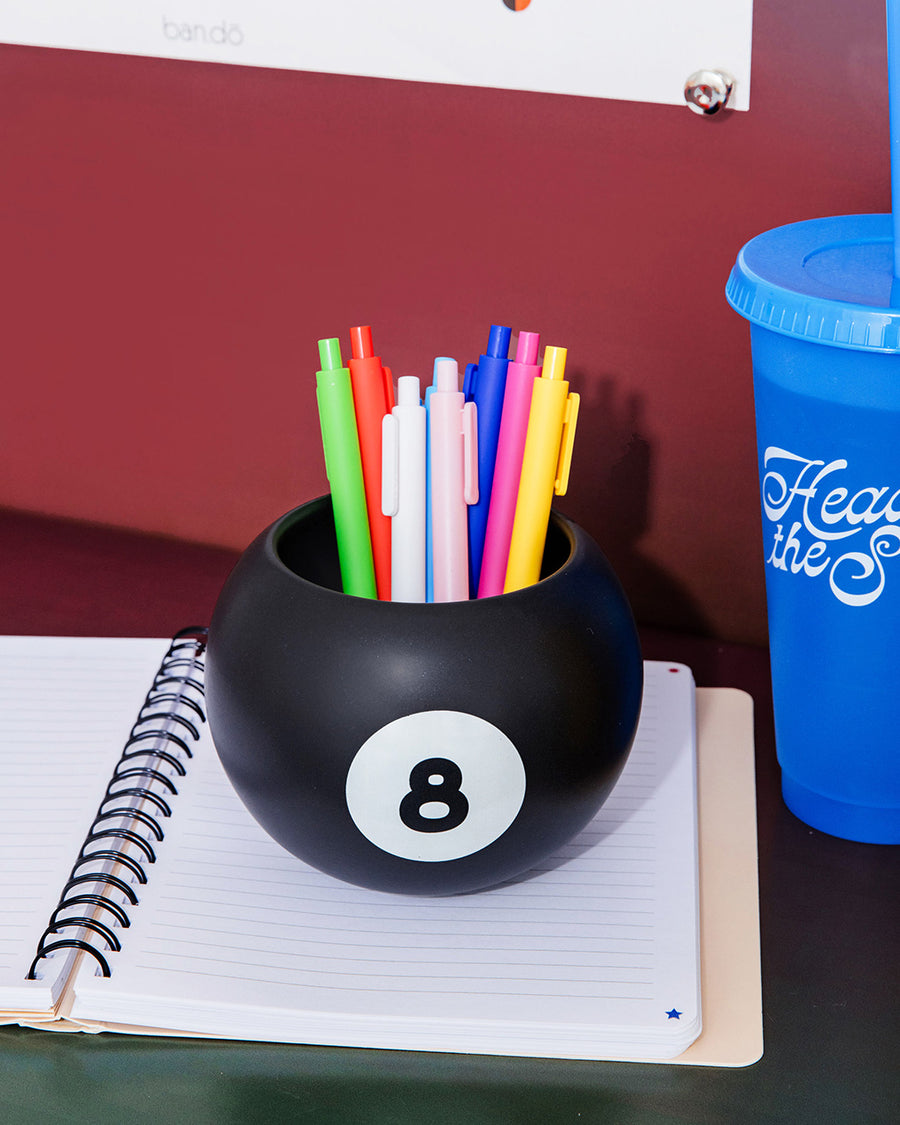 black magic 8 ball shaped vase with pens inside on a desk