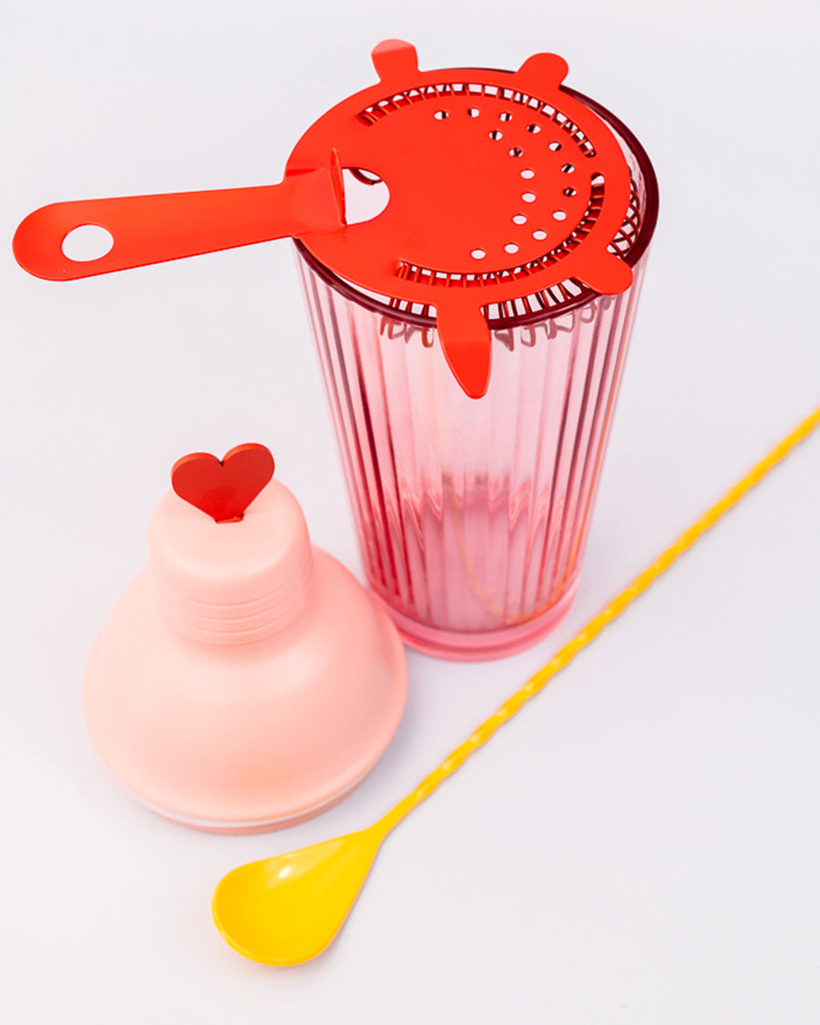 pink bar shaker with red heart top, red strainer, and yellow stirring stick with strainer on top