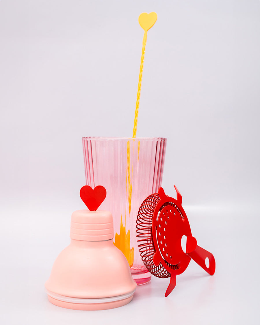 pink bar shaker with red heart top, red strainer, and yellow stirring stick