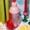 pink bar shaker with red heart top, red strainer, and yellow stirring stick on a pink checkered table