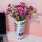 rolled newspaper shaped vase with white flowers inside on a desk