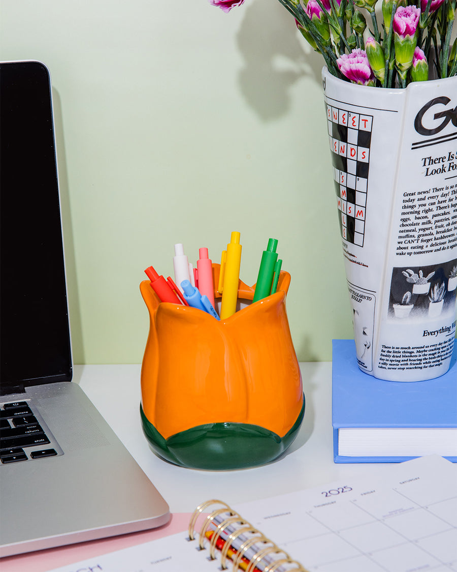 orange tulip shaped pencil holder with various pens inside on a desk