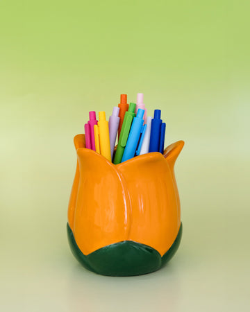 orange tulip shaped pencil holder with various pens inside