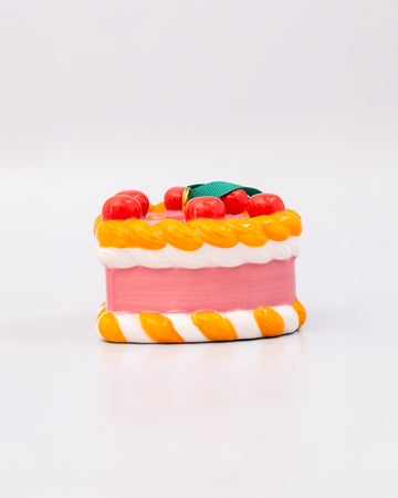 side view of ceramic pink cake shaped ornament with orange and white trim and 'cherries on top' 