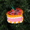 ceramic pink cake shaped ornament with orange and white trim and 'cherries on top' in a tree